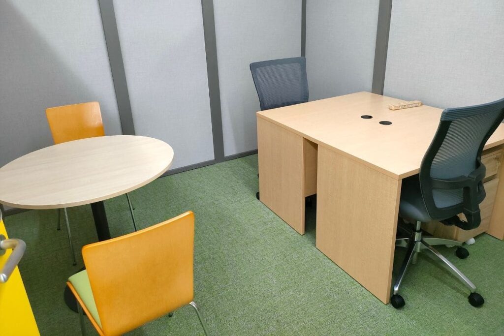 シェアオフィス内にある対面の作業用机と面談用の丸テーブルと椅子