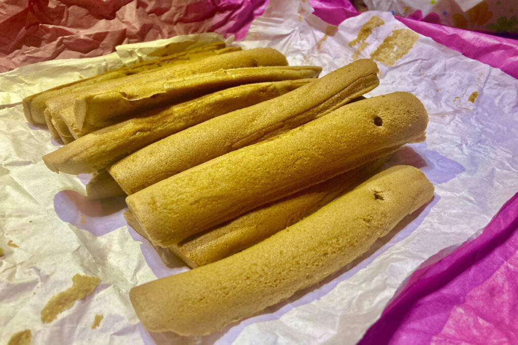 ピンクと白の包み紙の上に茶色くて細長いお菓子「ぽっぽ焼き」が載っています