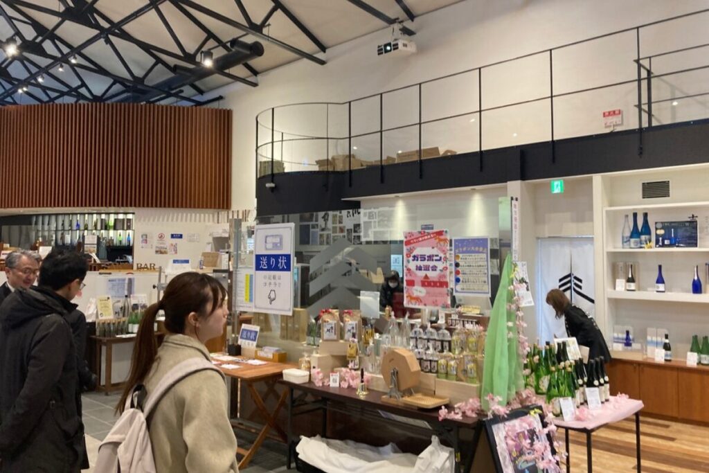 販売スペースが写っています。丈夫に通路があり、その下にレジがあります。中央には商品の置かれたテーブルがあり、ガラポンがあります。