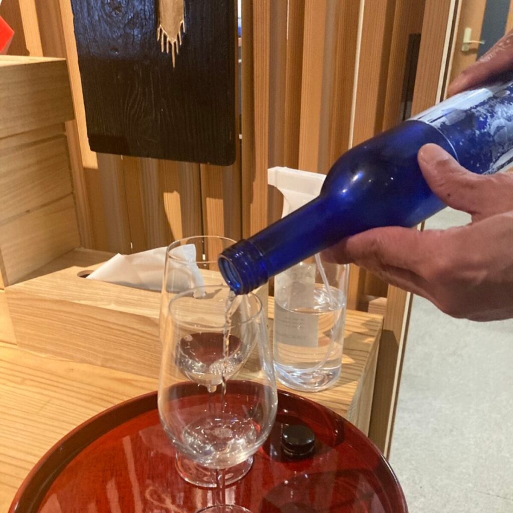 青色の瓶からグラスに酒を注いでいます。