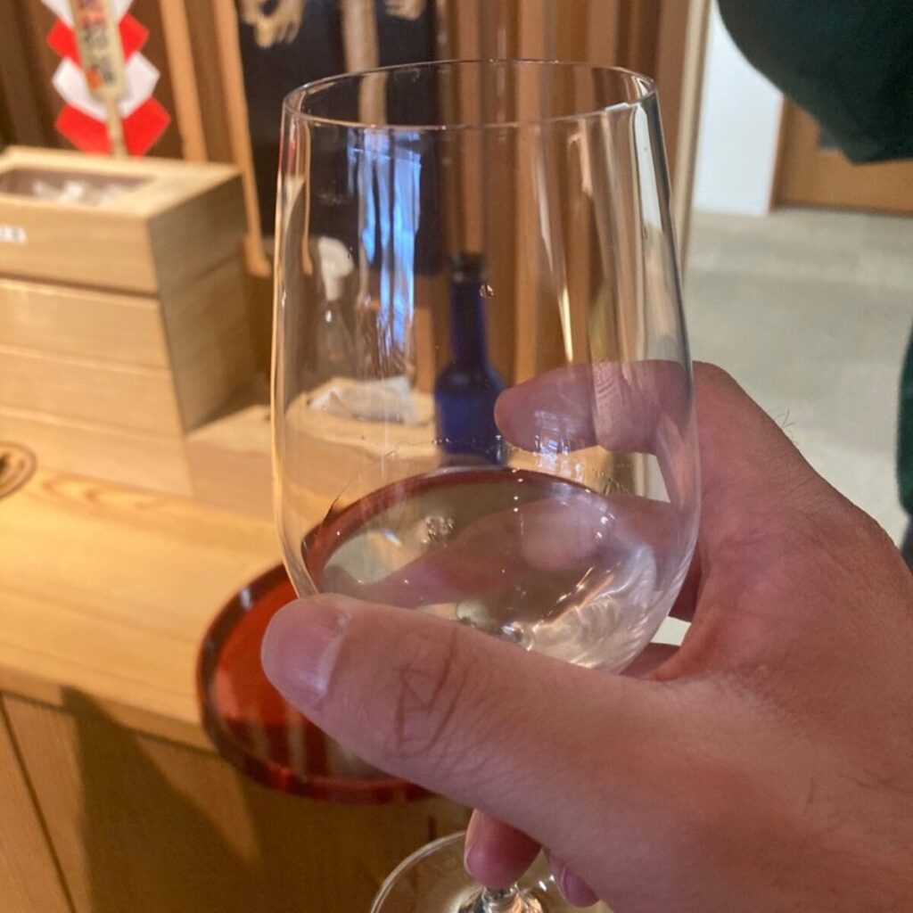 透明なグラスにやや濁りのある液体が入っており、右手でそれを持っています。