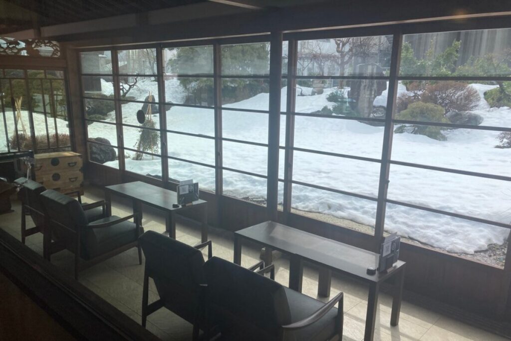 大きな窓からが見えるように、テーブルと椅子が置かれています。窓の外は庭園で、雪が積もっています。