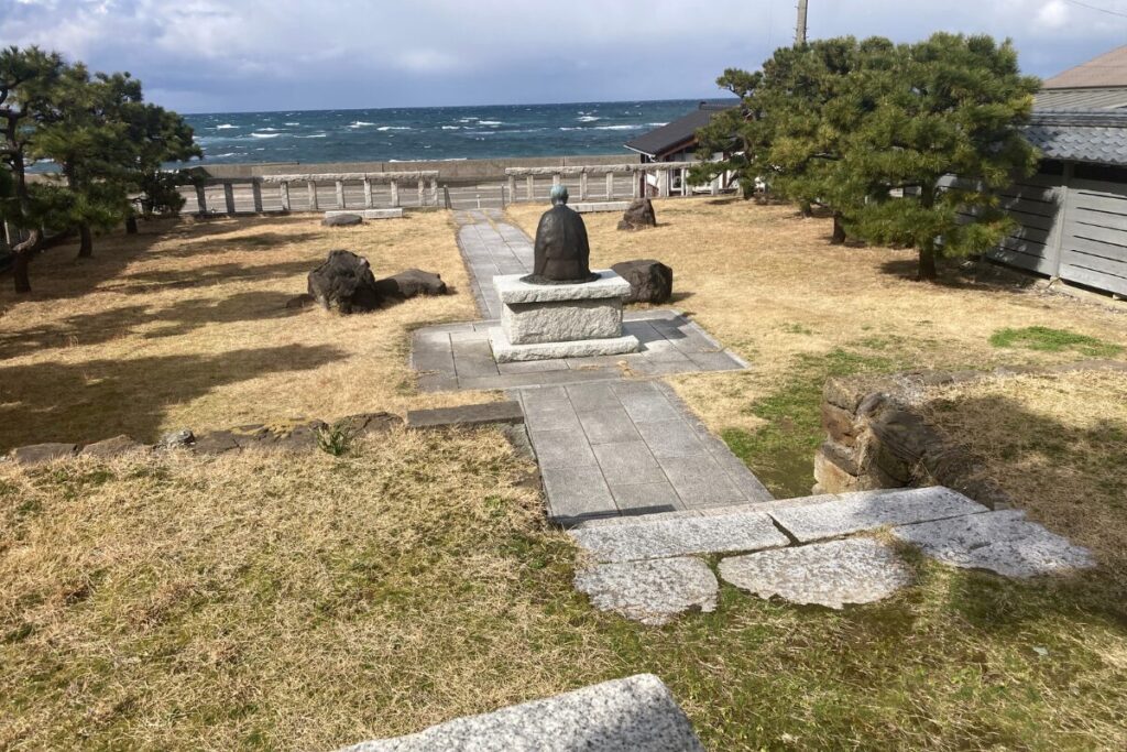 画面中央に良寛像の後ろ姿が見えます。奥には海が見えます。