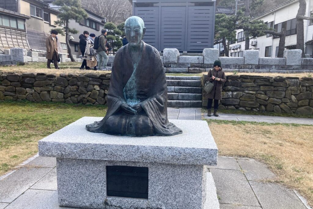 良寛像の後ろで良寛堂を観察する人々が映っています。