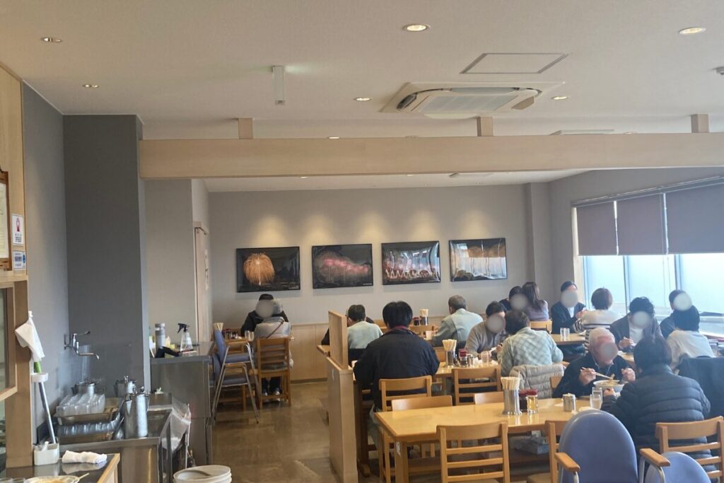 飲食店の中でさまざまな人たちが座ってラーメンを食べています。