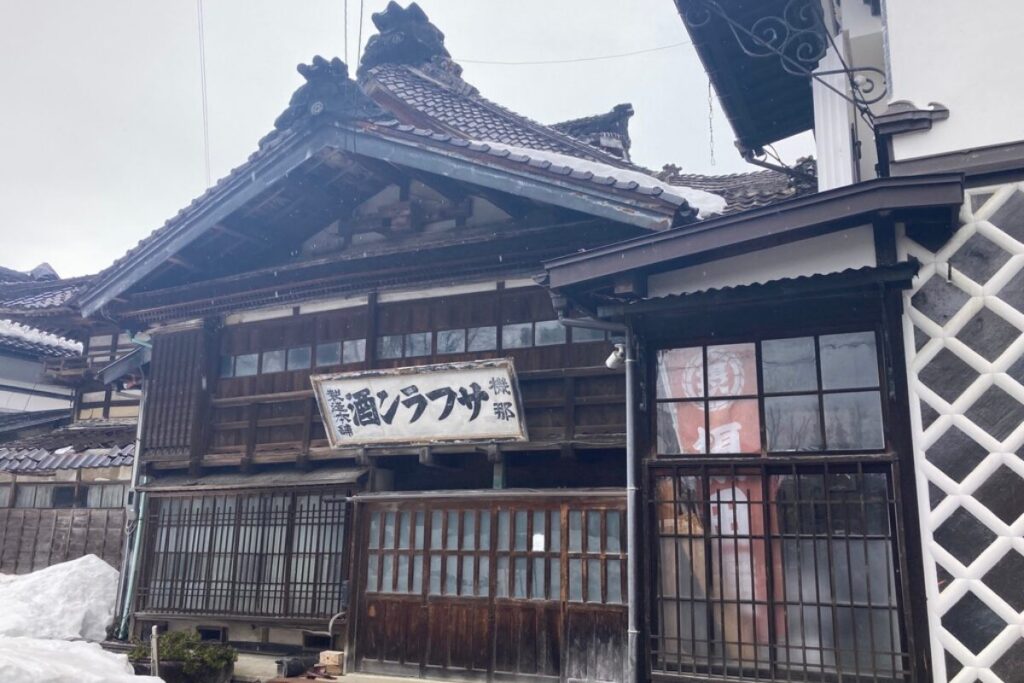 古い住宅が写っていて、玄関の上に「機那サフラン酒製造本舗」と書かれた看板がかかっています。