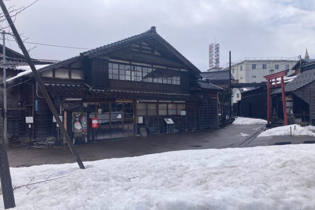 古い木造の家屋、その手前には小道と残っている雪が写っています。