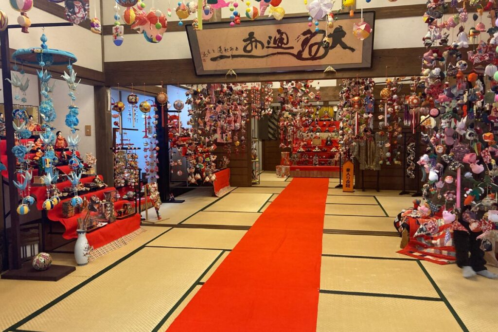 畳の部屋で中央に赤いカーペットが敷かれ、左右と中央奥に雛飾りが置かれています。