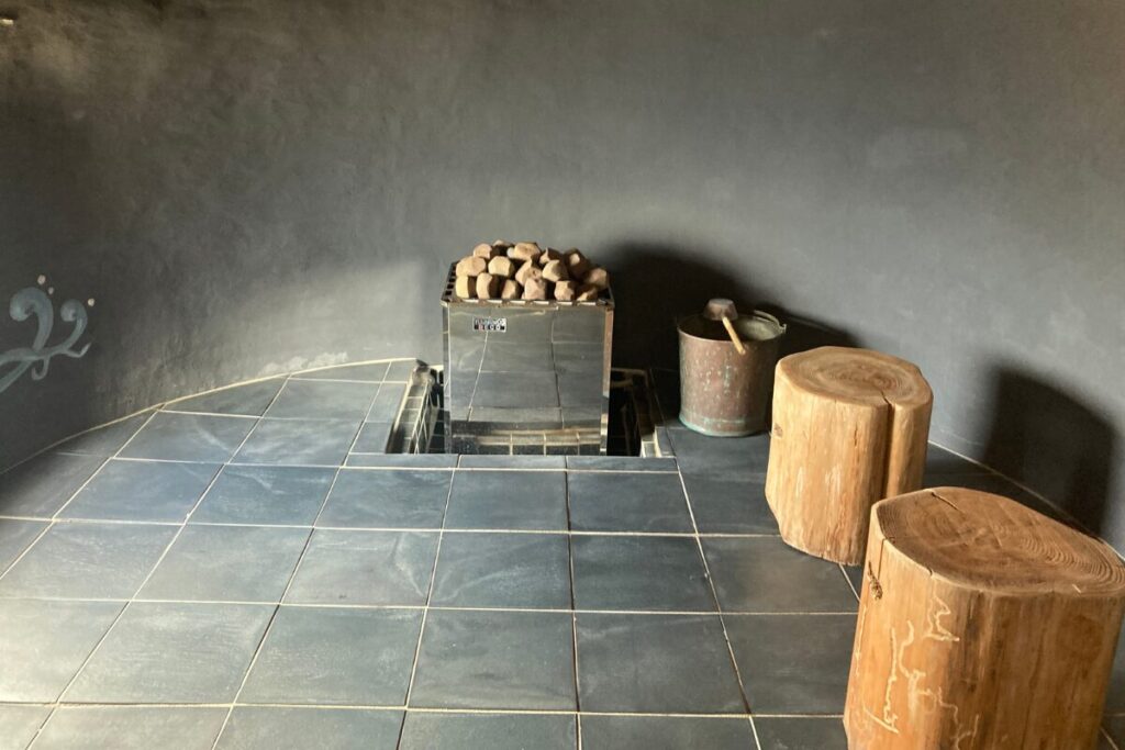 サウナ室で、真ん中にサウナストーン、右側に木の椅子が2つ並んでいます。