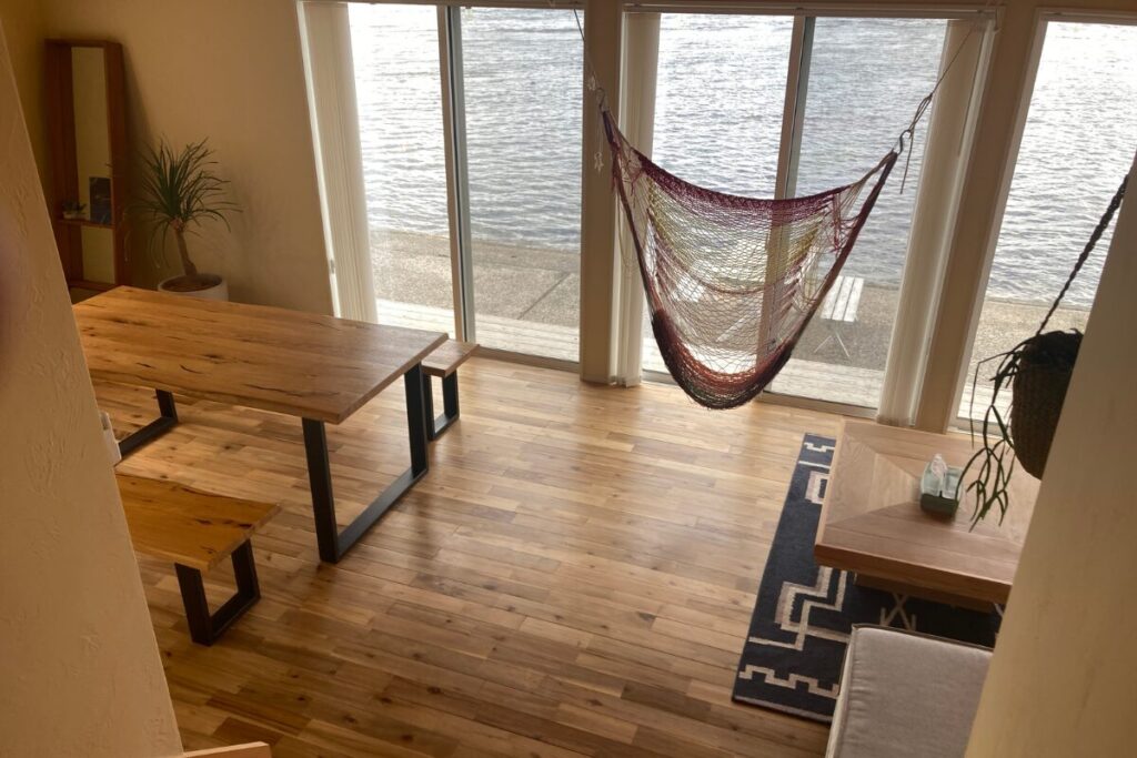 フローリングの部屋で左側にテーブルと椅子、右側にハンモックと低いテーブルがあります。