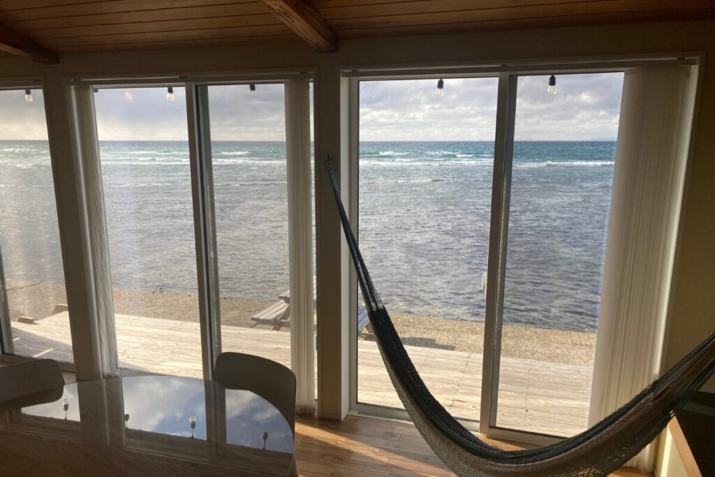 室内から海を見渡すパノラマビュー。大きな掃き出し窓の前にハンモックが吊るされ、外にはウッドデッキが広がっています。