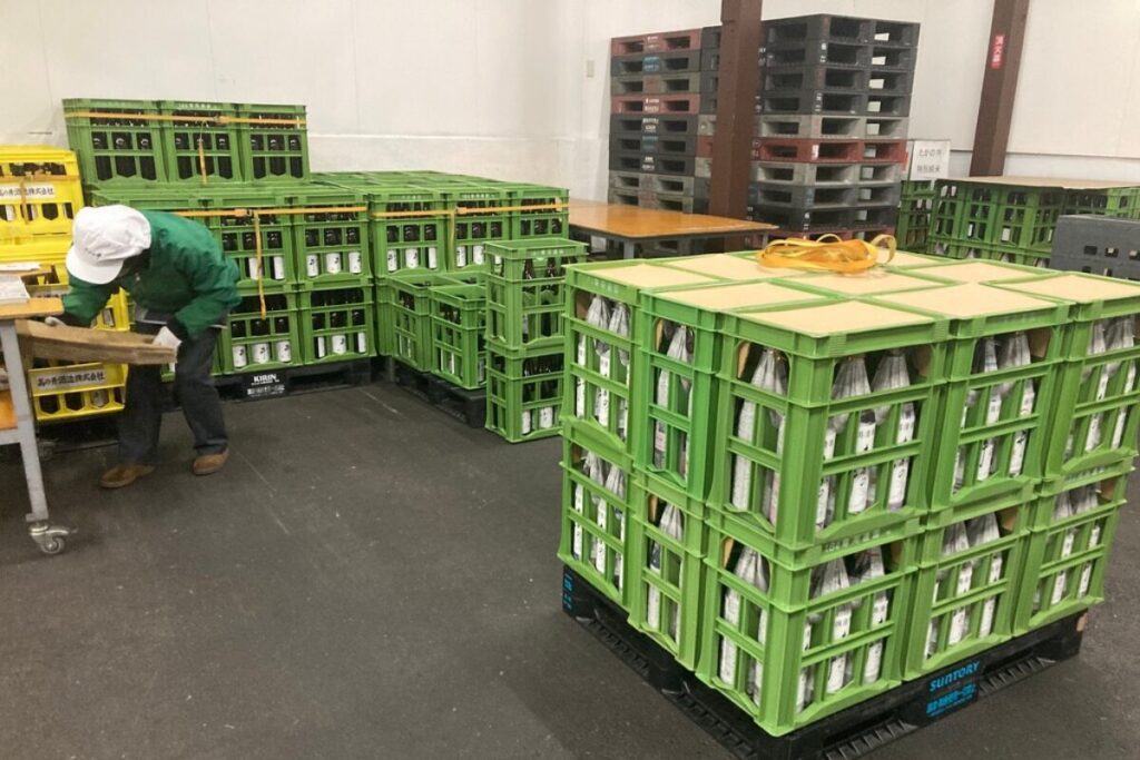 緑色のケースに酒瓶が入っていて、まとめられています。作業着をきた人が仕分け作業をしています。