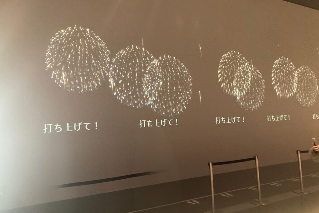 大きなプロジェクターの画面に「打ち上げて！」というテキストと花火のアニメーションが写っています。