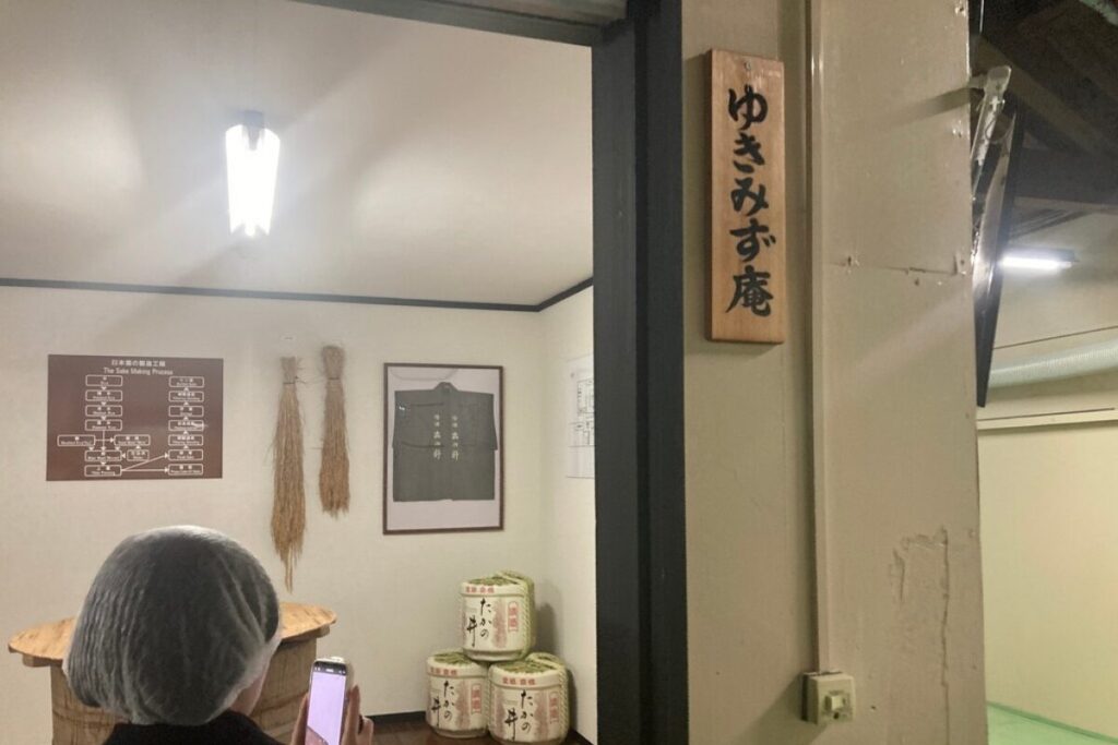部屋の入り口で、奥には日本酒の製造工程表と稲藁、隅に酒樽があります。部屋の外の壁の札には「ゆきみず庵」と書いてあります。