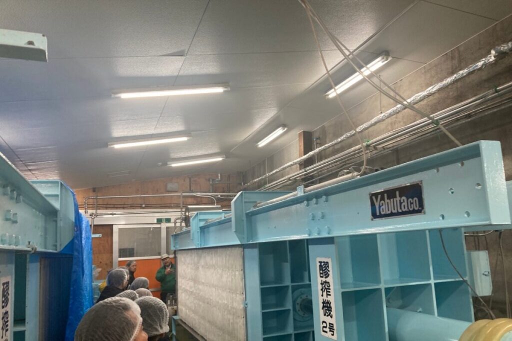 醪搾機と書かれた大きな水色の機械があります。天井には蛍光灯があります。