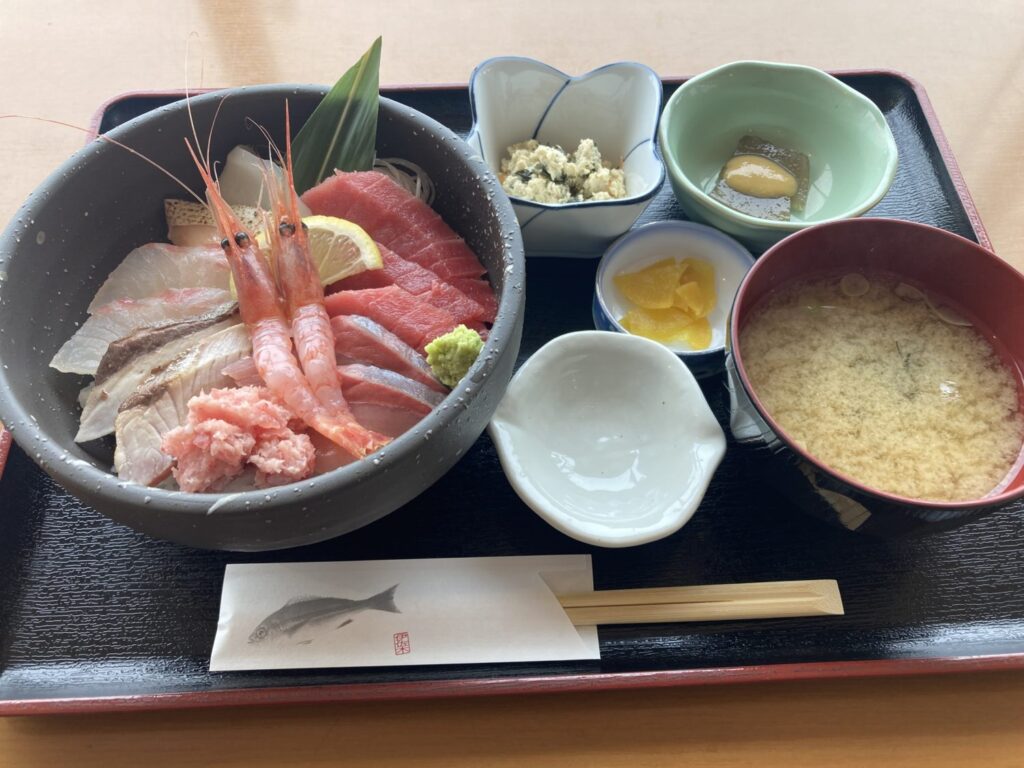 海鮮丼です。右側に味噌汁のお椀、右上に小鉢が3つあり、たくあん、おかき、練り物と並んでいます。