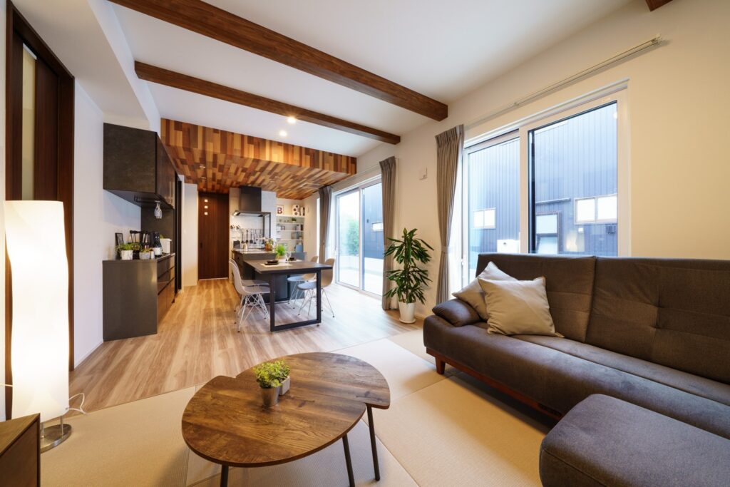 リビングを撮影した写真です。中央に四人がけの黒いテーブルがあり、その周囲に白い椅子が4つ置いてあります。その手前に丸テーブルがあり、右側に大きなソファが設置されています