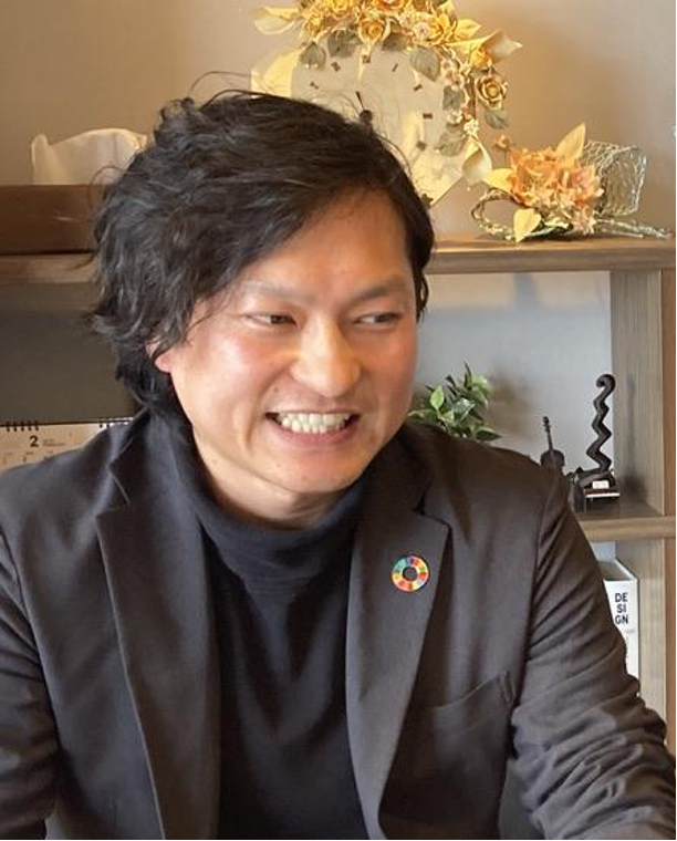 ジャケットを着た男性が微笑みを浮かべながら語っている様子です。