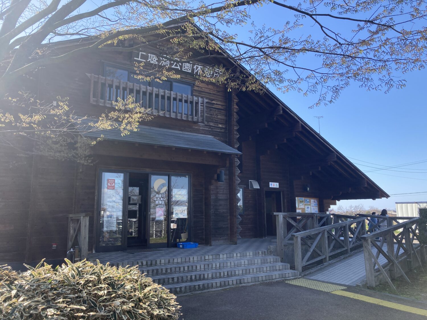 木製のログハウスです。「上堰潟公園休憩所」という看板が入り口の上に貼ってあります。