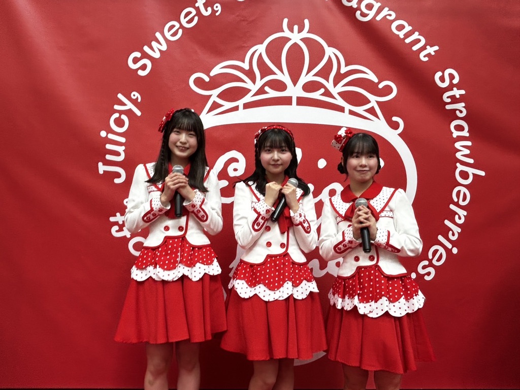 赤い壁紙をバックに、赤と白を組み合わせたデザインの衣装を着た3名の女性が写っています。